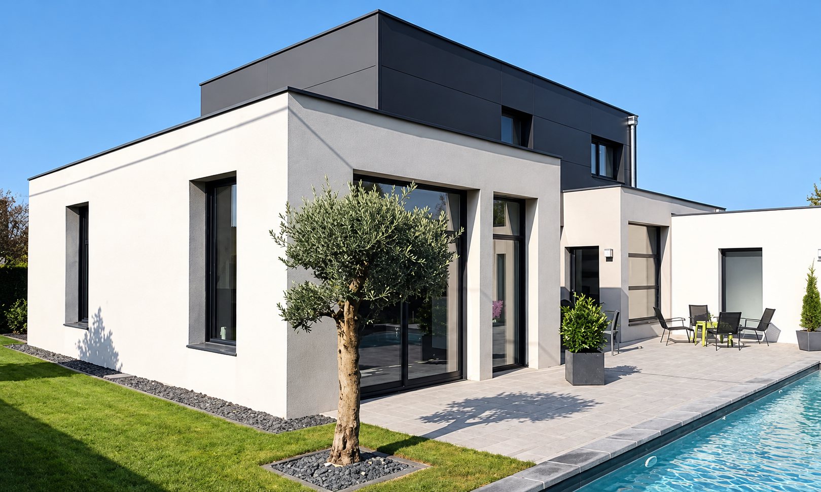 Maison contemporaine aux volumes cubiques blancs et gris, avec un olivier sur la pelouse, une terrasse équipée de chaises et une piscine au premier plan.