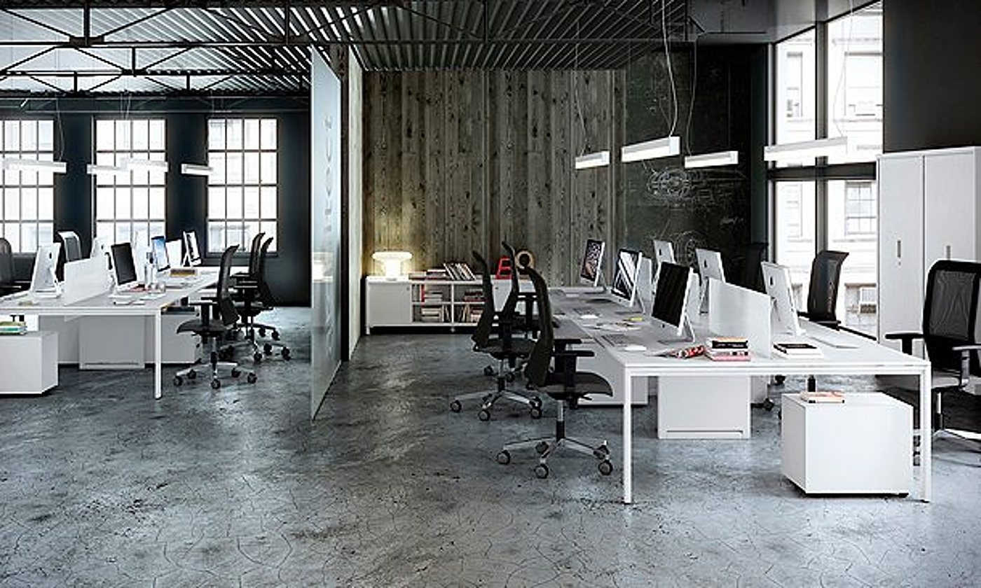 Vaste espace de bureau de style industriel avec de longs bureaux blancs, des fauteuils ergonomiques noirs, des écrans d’ordinateur et un sol en béton ciré.